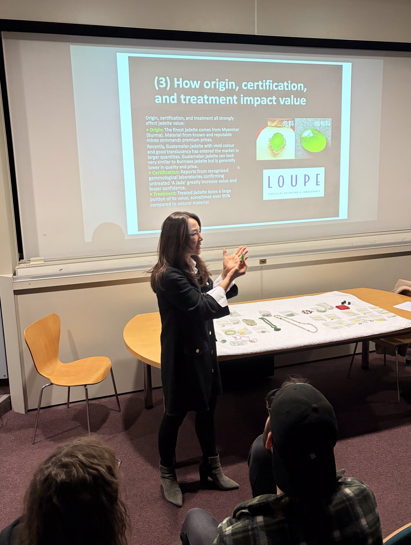 Kehan Li mid-lecture, gesturing in front of a slide titled "How origin, certification, and treatment impact value".